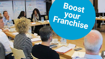 Seminarsituation mit Teilnehmern, darüber ein Sticker mit der Aufschrift: Boost your Franchise